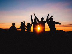 A group of people jumping and waving their hands to a sunrise next to each other