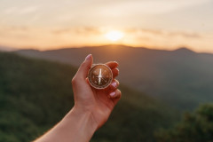 A hand holding a compass with mountains and sunrise in the background