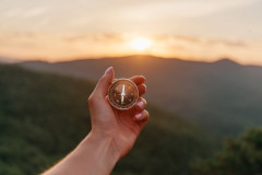A hand holding a compass with mountains and sunrise in the background