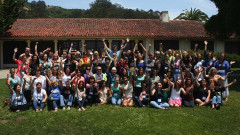 A group photo of everyone sitting on the grass, waving their hands, and smiling to the camera.