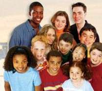 A group of eleven diverse children and two adults smiling at the camera. The adults stand behind the children, who are arranged in two rows in front. The background is neutral and slightly blurred, focusing attention on the people.